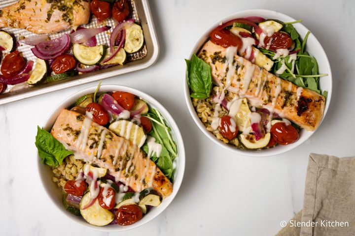 Roasted Garlic Salmon and Vegetable Farro Bowls with a garlic drizzle sauce in two bowls.
