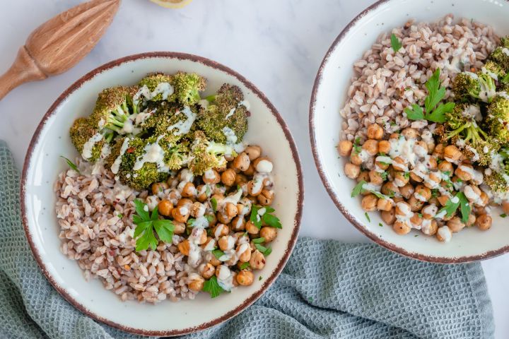 Garlic tahini broccoli bowls with cooked farro, roasted broccoli, roasted chickpeas, and tahini sauce in two bowls.