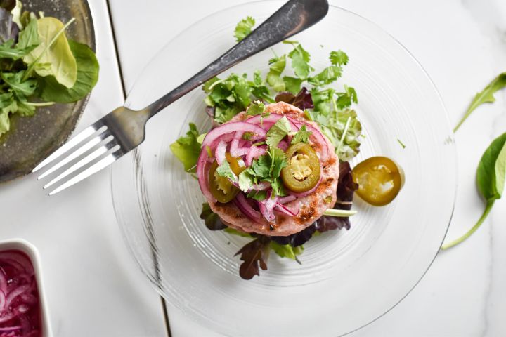 Green chile turkey burger with pickled red onions and greens on a plate with pickled jalapenos.