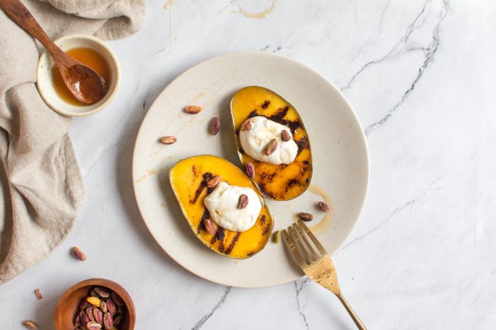 Grilled mango sliced in half on a plate with a dollop of yogurt, honey, and pistachios.