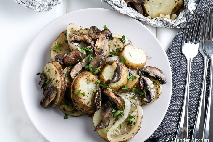 Grilled potatoes with onions, mushrooms, and butter on a plate. 