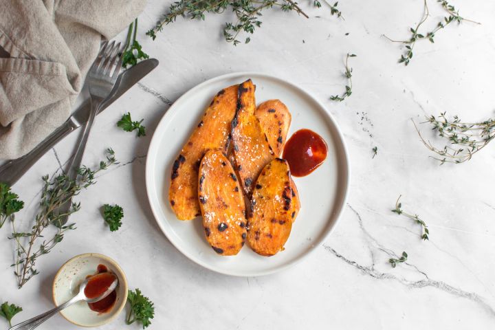 Grilled sweet potatoes with olive oil and spices on a plate with fresh thyme.