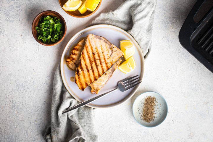 Grilled swordfish with garlic, lemon, and herbs on a plate with fresh parsley.