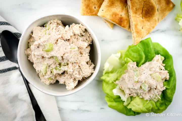 Healthy tuna salad with celery in a bowl with lettuce and pita triangles on the side.