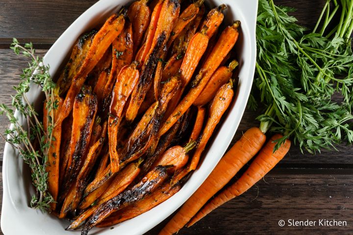 Honey Balsamic Carrots in a white dish with fresh carrots on the side.