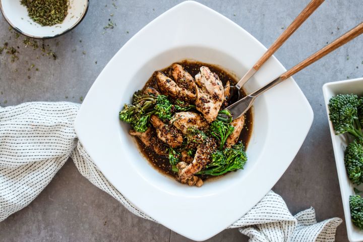 Honey mustard chicken with broccolini in a white bowl with a honey balsamic sauce poured on top.