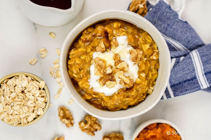 Pumpkin oatmeal with walnuts, maple syrup, and yogurt in a bowl with oats on the side.