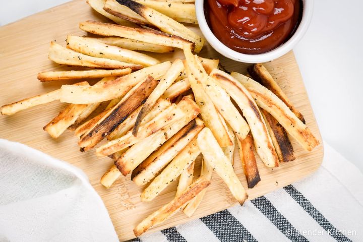 Parsnip fries cut into match sticks with spices on a wooden cutting board with kethcup.