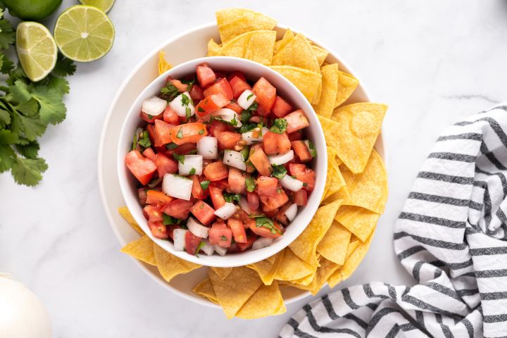 Pico de gallo with diced tomatoes, white onion, cilantro, jalapeno, and lime juice in a white bowl with tortilla chips on the side.