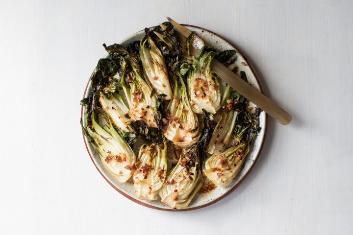 Roasted bok choy with soy sauce, garlic, ginger, and sesame seeds on a plate with a gold fork.