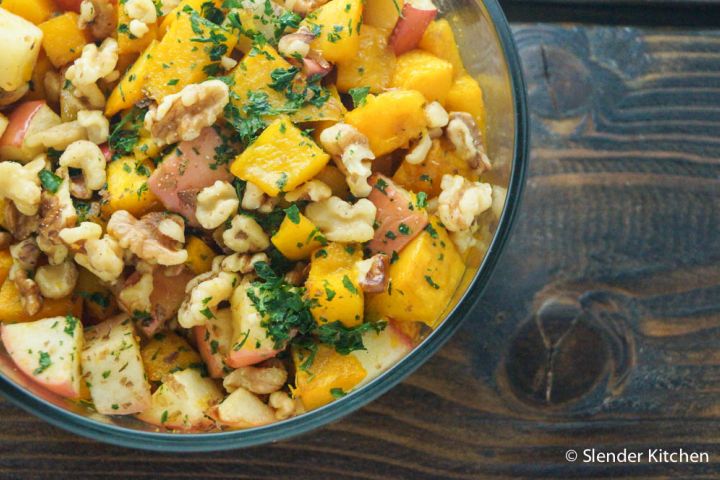 Roasted butternut squash and apples on a plate topped with walnuts and parsley.