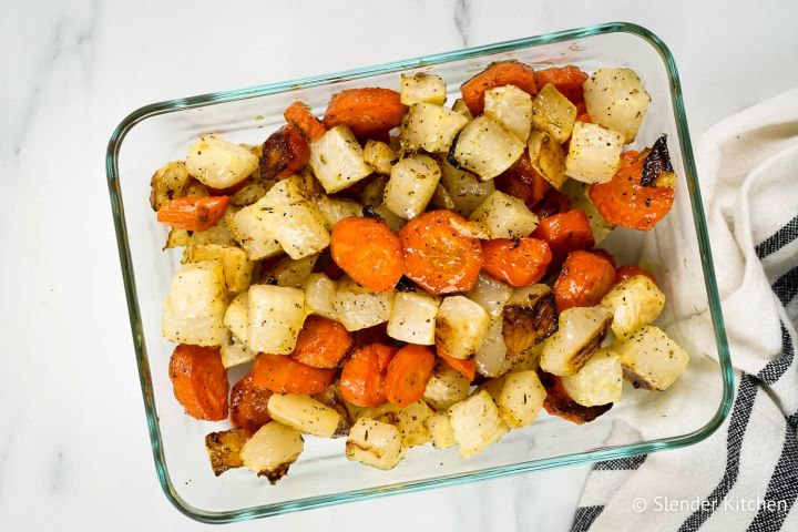 Roasted carrots and turnips with herbs in a glass container.