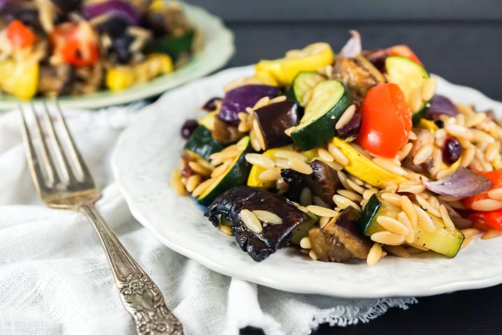 Roasted vegetables with eggplant, zucchini, summer squash, and onions on a plate with cooked orzo.