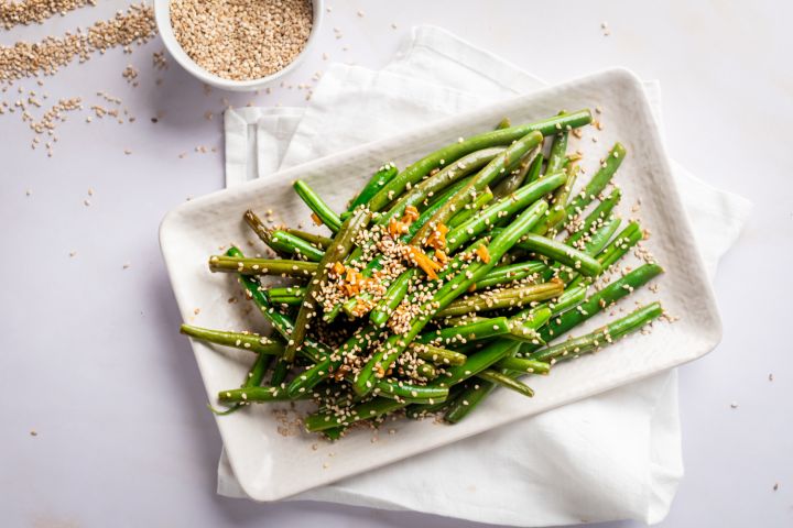 Sesame green beans on a plate with sautéed garlic, sesame seeds, and soy sauce.