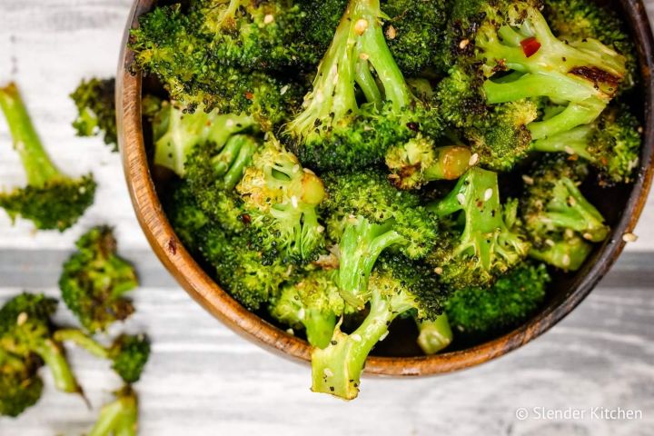 Sesame broccoli with sesame oil, sesame seeds, and soys sauce in a bowl with red pepper flakes and garlic.