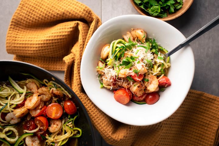 Healthy shrimp scampi zoodles with garlicky shrimp, tomatoes, Parmesan cheese, zucchini noodles, and parsley in a bowl.