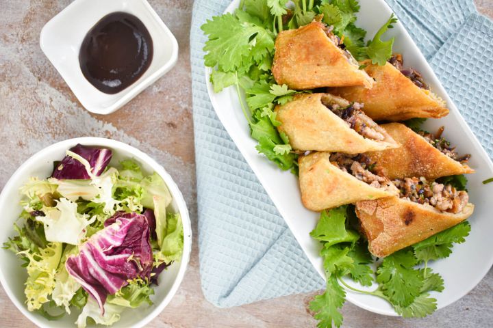 Baked egg rolls with cabbage, carrots, and ground chicken cut in half on a plate with oyster sauce.