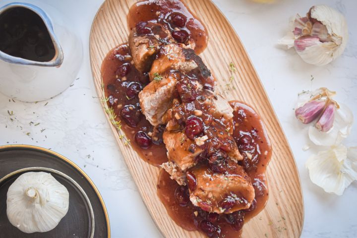 Slow cooker cranberry pork roast with sliced pork and a cranberry honey sauce on a wooden plate.