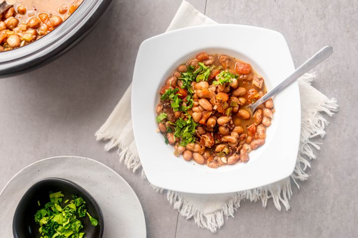 Slow cooker frijoles charros, cowboy beans, in a bowl with creamy pinto beans, jalapenoes, tomatoes, onions, and fresh cilantro.
