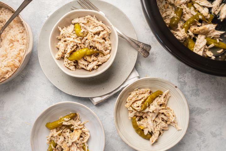 Slow cooker pepperoncini chicken shredded in three bowls with rice on the side and whole pepperoncini peppers.