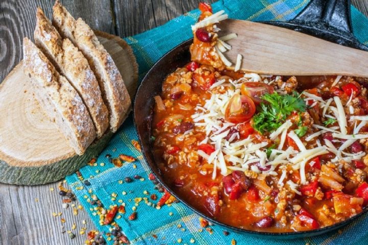 Pepperoni pizza chili in a blue bowl with slices of bread on the side.