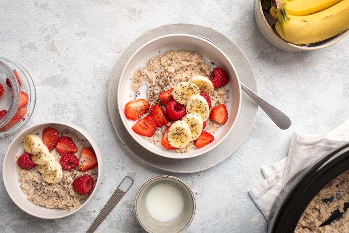 Slow cooker steel cut oatmeal in two bowls with bananas, raspeberries, strawberries, and milk.