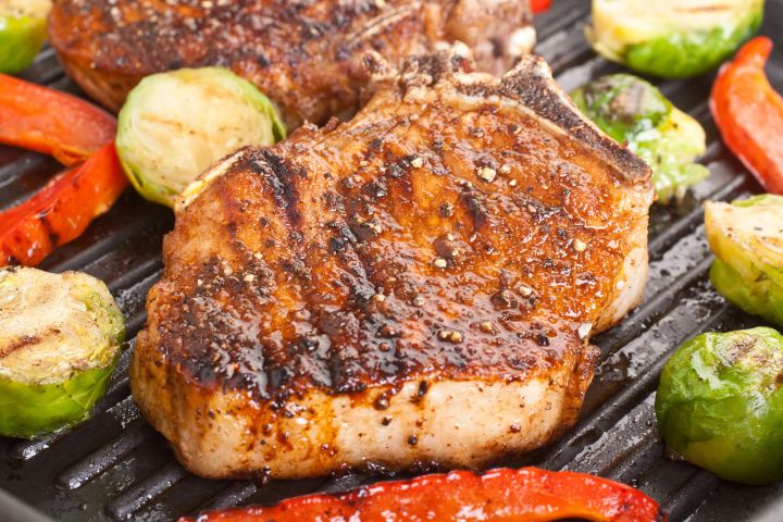 Grilled pork chops with southwestern seasoning on a grill with brussels sprouts and peppers.