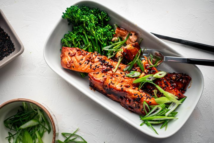 Teriyaki salmon baked in the oven and served with green onions, sesame seeds, and broccoli on the side.