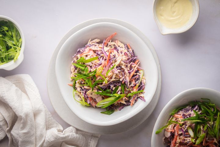 Tricolor coleslaw with red cabbage, green cabbage, and carrots in a bowl with yogurt dressing and green onions.