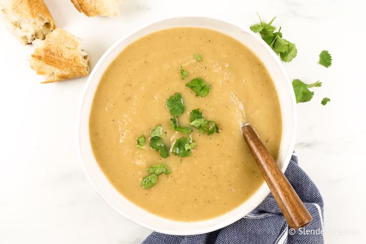Turnip soup with potatoes in a bowl with fresh herbs, a wooden spoon, and fresh bread.