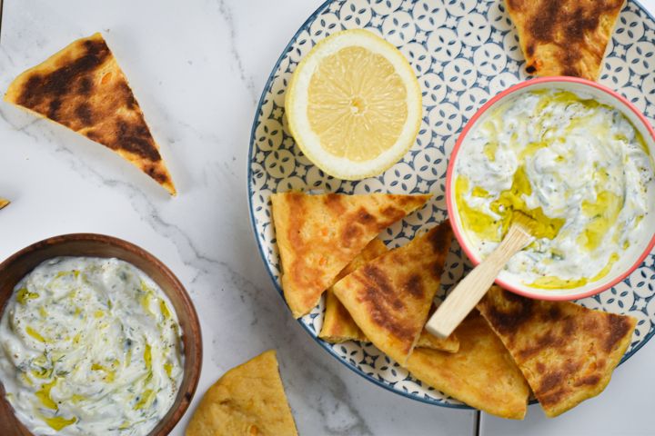 Tzatziki made with Greek yogurt, cucumbers, lemon, garlic, and dill in a bowl with pita wedges on the side.