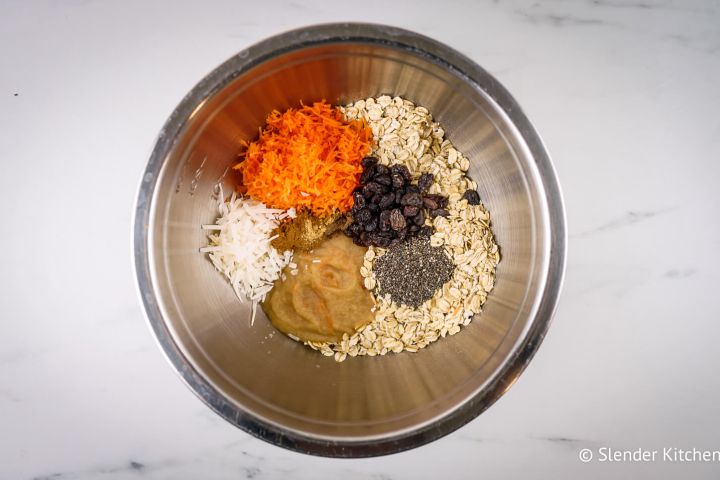 Rolled oats, carrots, raisins, chia seeds, coconut, and spices in a metal bowl.