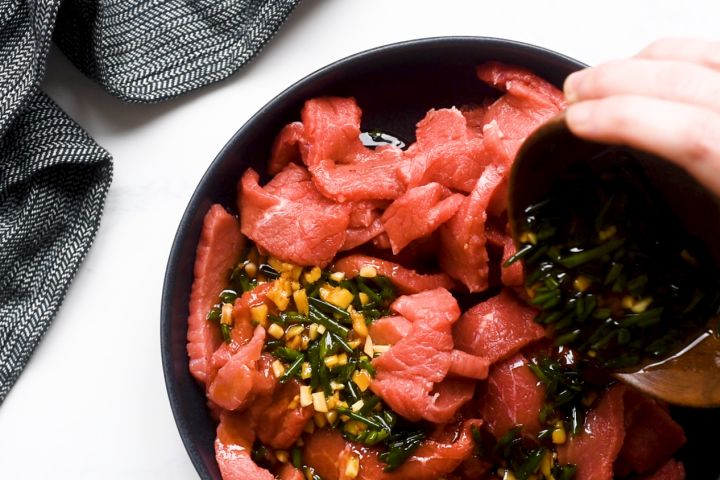 Raw sliced beef with marinade in a bowl with green onions.