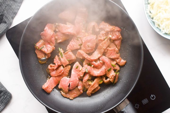 Beef being stir fried in a hot skillet.