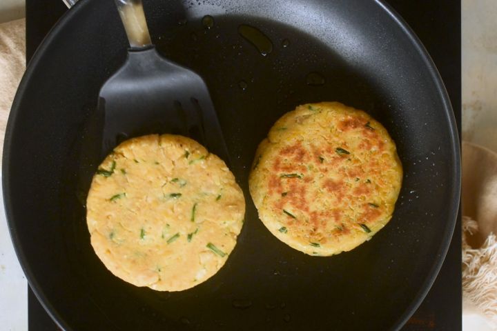 Chickpea burgers being cooked in a cast iron skillet.