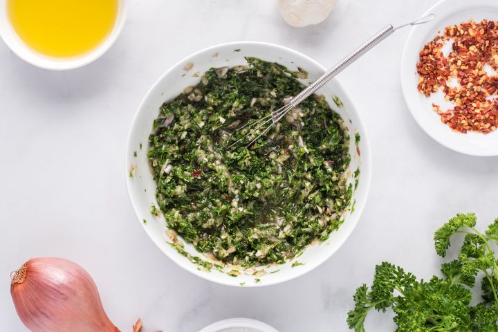 Chimichurri sauce in a small white bowl with a whisk.
