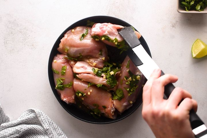 Raw chicken thighs being marinated with cilantro and lime.