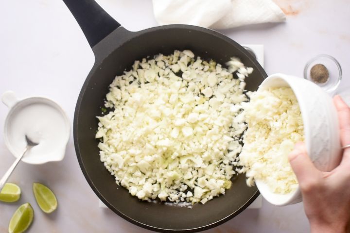Cauliflower rice cooking in a skillet with garlic and ginger.
