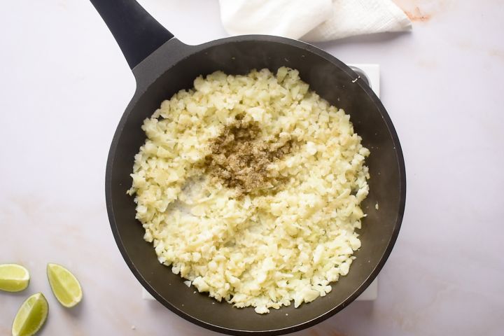Cauliflower rice with coconut milk cooking in a skillet.