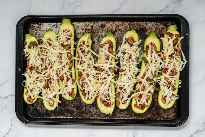 Zucchini boats filled with fajita bean mixture and cheese on a baking dish.