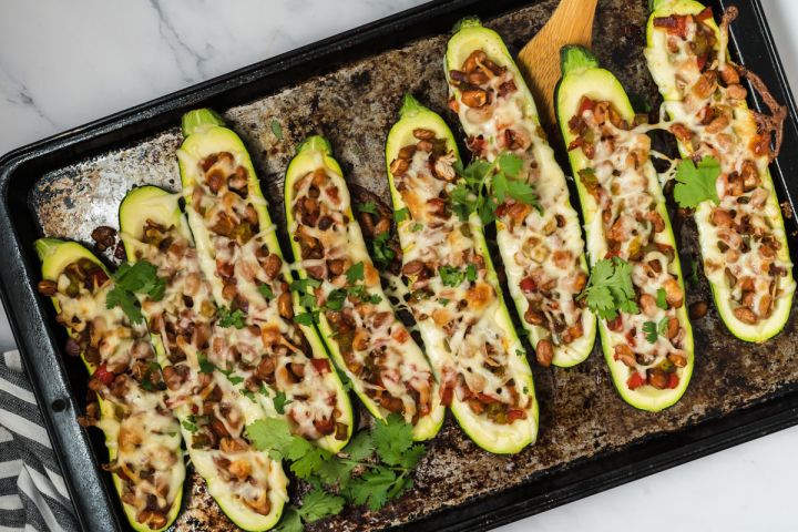 Fajita zucchini boats on a baking sheet with beans, peppers, onions, and melted cheese.