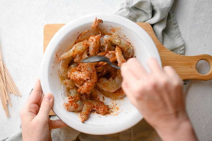 Shrimp being marinated in lemon juice and spices in a bowl.