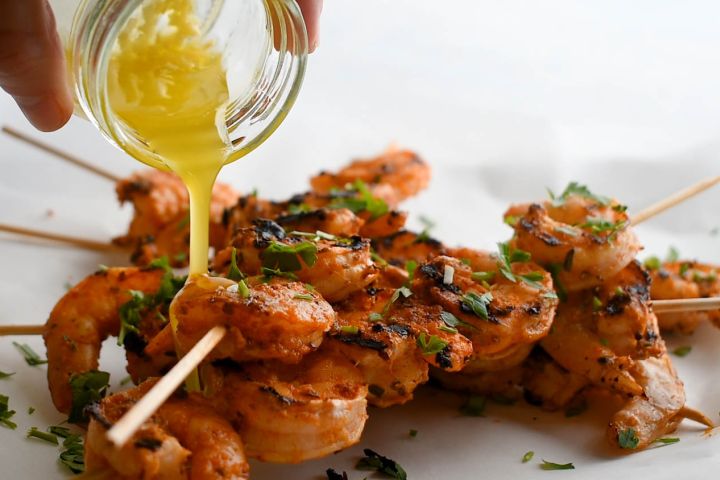 Grilled shrimp on skewers with melted butter being poured on top.