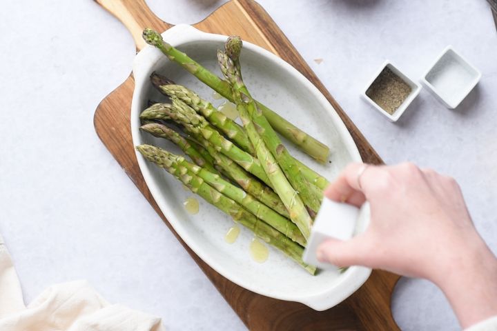 Asparagus in a dish being drizzled with olive oil.