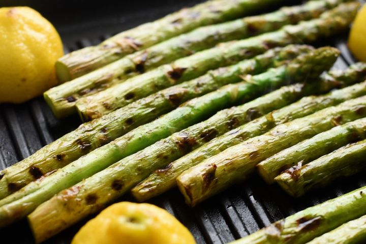 Asparagus stalks on the grill with fresh lemon halves.