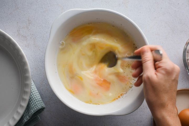 Eggs, milk, salt, and pepper being whisked in a bowl.