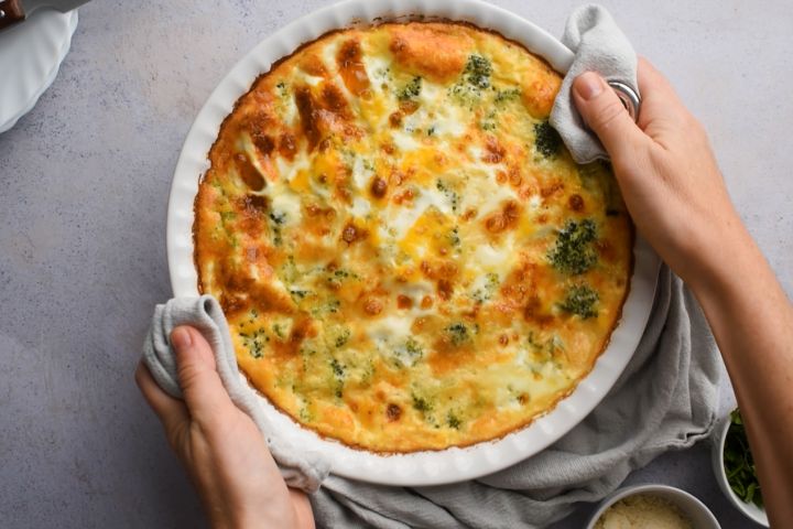 Ham and cheese frittata with broccoli being taken out of the oven by two hands.