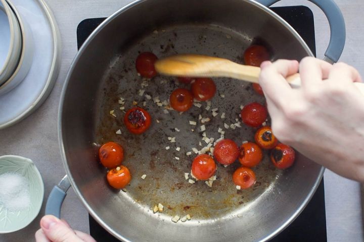 Cherry tomatoes and garlic cooking in a pot.