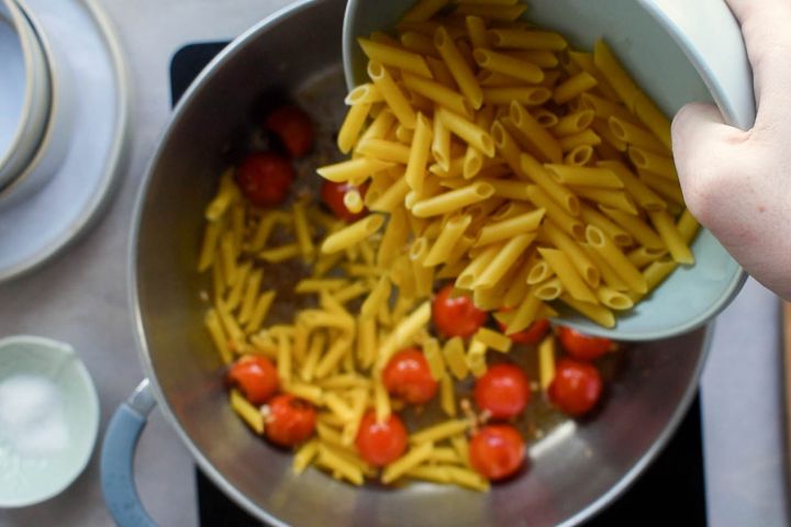 Pasta being added to cherry tomatoes in a pot.