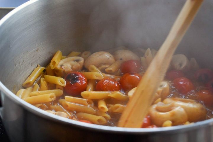 Tomato basil pasta cooking in a pot with a spoon.